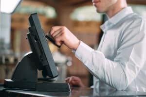 A server wearing a white button-up shirt is swiping a credit card at a POS terminal in a restaurant setting.