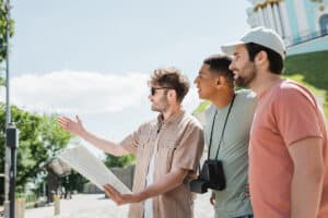 A tour guide is holding a map and pointing in the distance as two tourists look onward.
