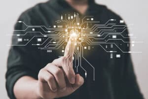 A person in a dark shirt touches a glowing circuit board with lines connecting various electronic components, featuring an icon of a brain labeled "AI Technology" at the center.